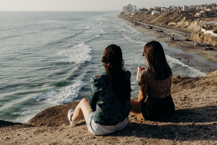 Backview Of Female Friends Relaxing By The Seaside