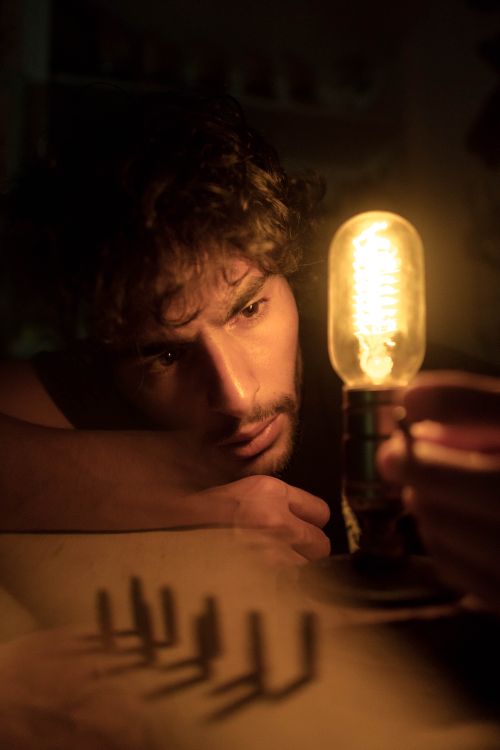 Free A man deeply contemplating while looking at a glowing light bulb, creating a warm atmosphere. Stock Photo