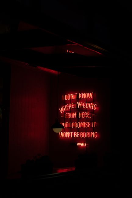 Red neon light with an inspiring message by Bowie on a dark wall, perfect for modern decor.