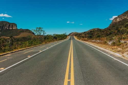 Free A scenic long road stretching through a desert landscape with hills under a vibrant blue sky. Stock Photo