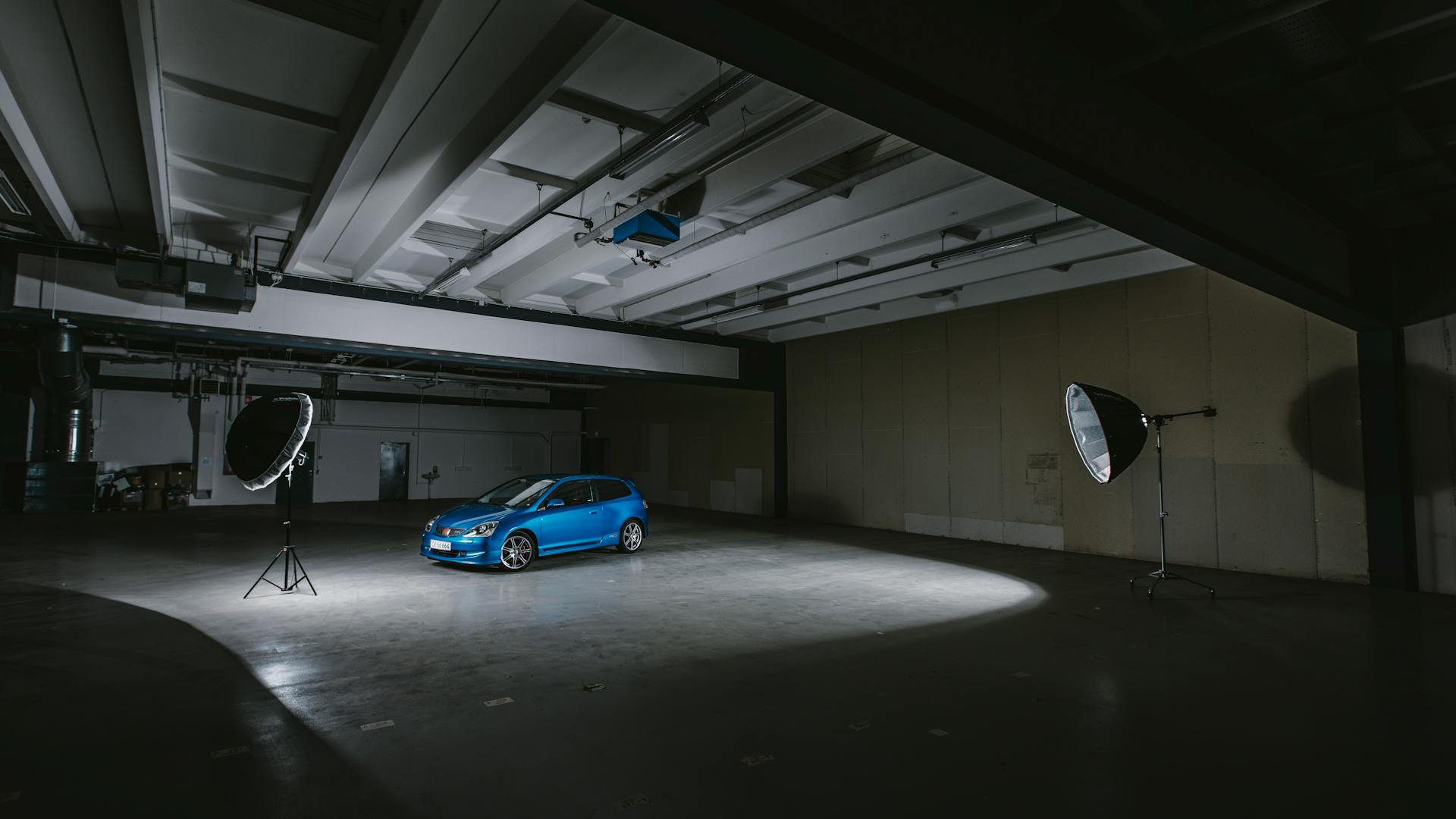 A blue car illuminated in a warehouse studio with professional lighting equipment.