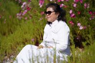 Woman in white attire relaxing in a vibrant flower field during sunny day.
