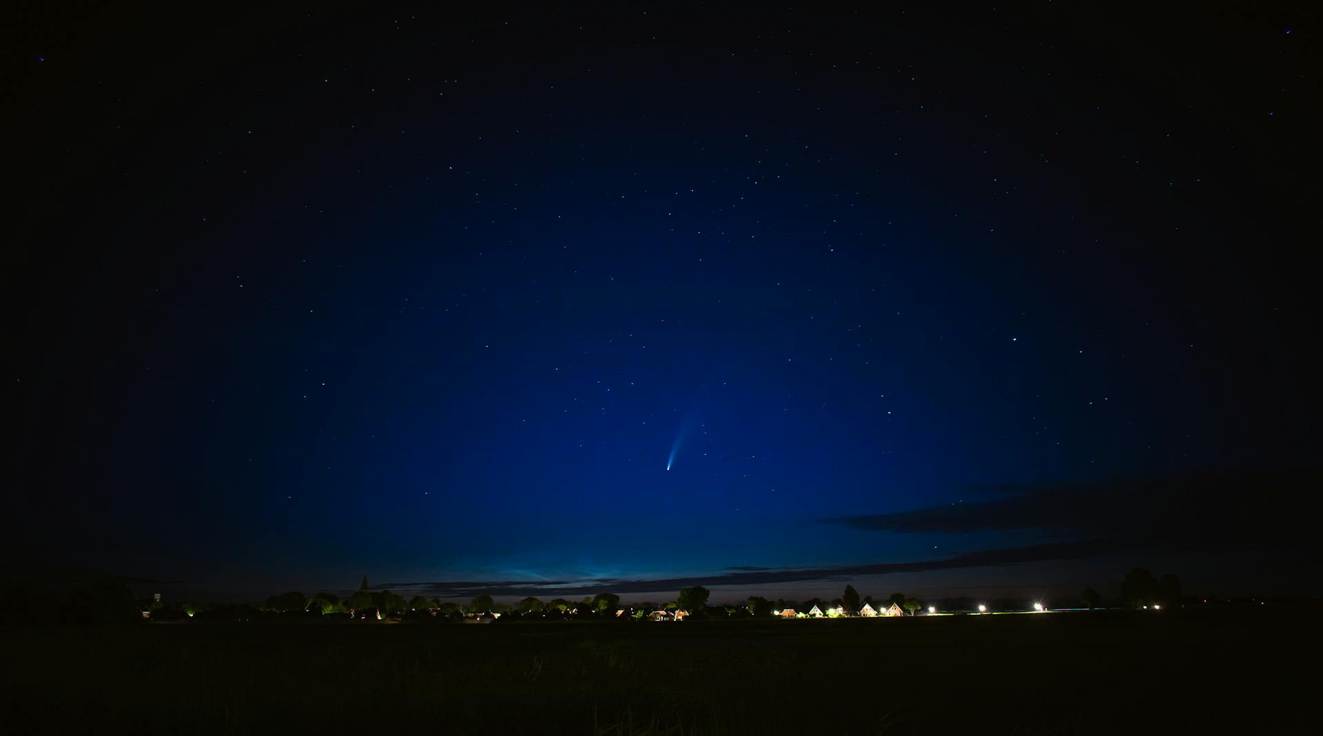 A stunning view of a comet streaking through the night sky over Groningen's horizon.