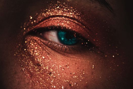 A stunning close-up of a human eye adorned with gold glitter makeup, showcasing beauty and fashion.