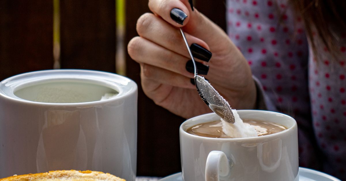 Mão colocando açúcar no café, representando o impacto do aumento do preço do açúcar no consumo diário