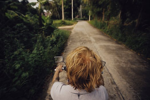 Rear view of a man with blonde hair riding a motorcycle down a country road.