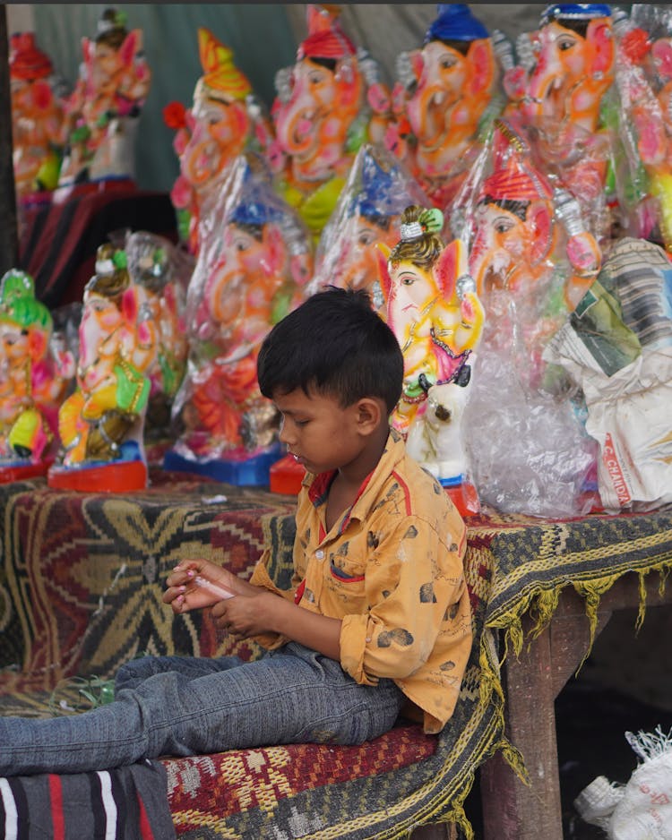 Child Playing In Front Of Ganesh Dolls