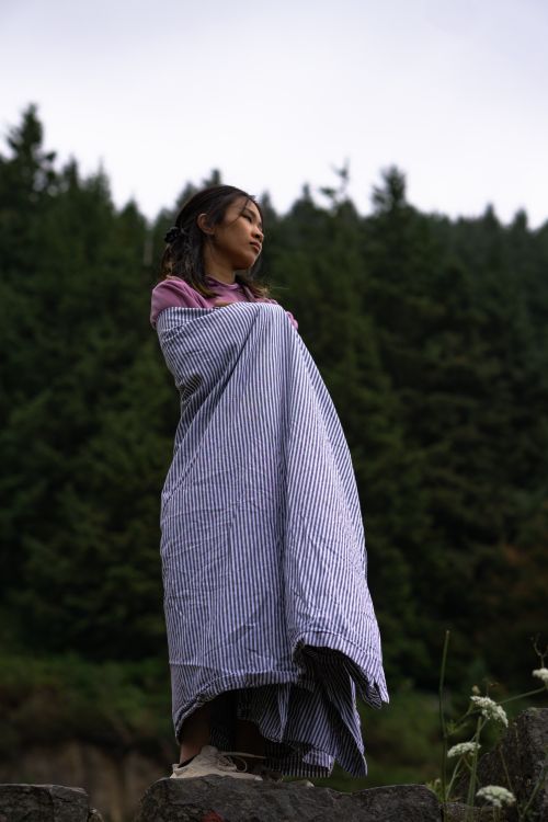 Free A young woman wrapped in a blanket stands in a forested area, enjoying an evening outdoors. Stock Photo