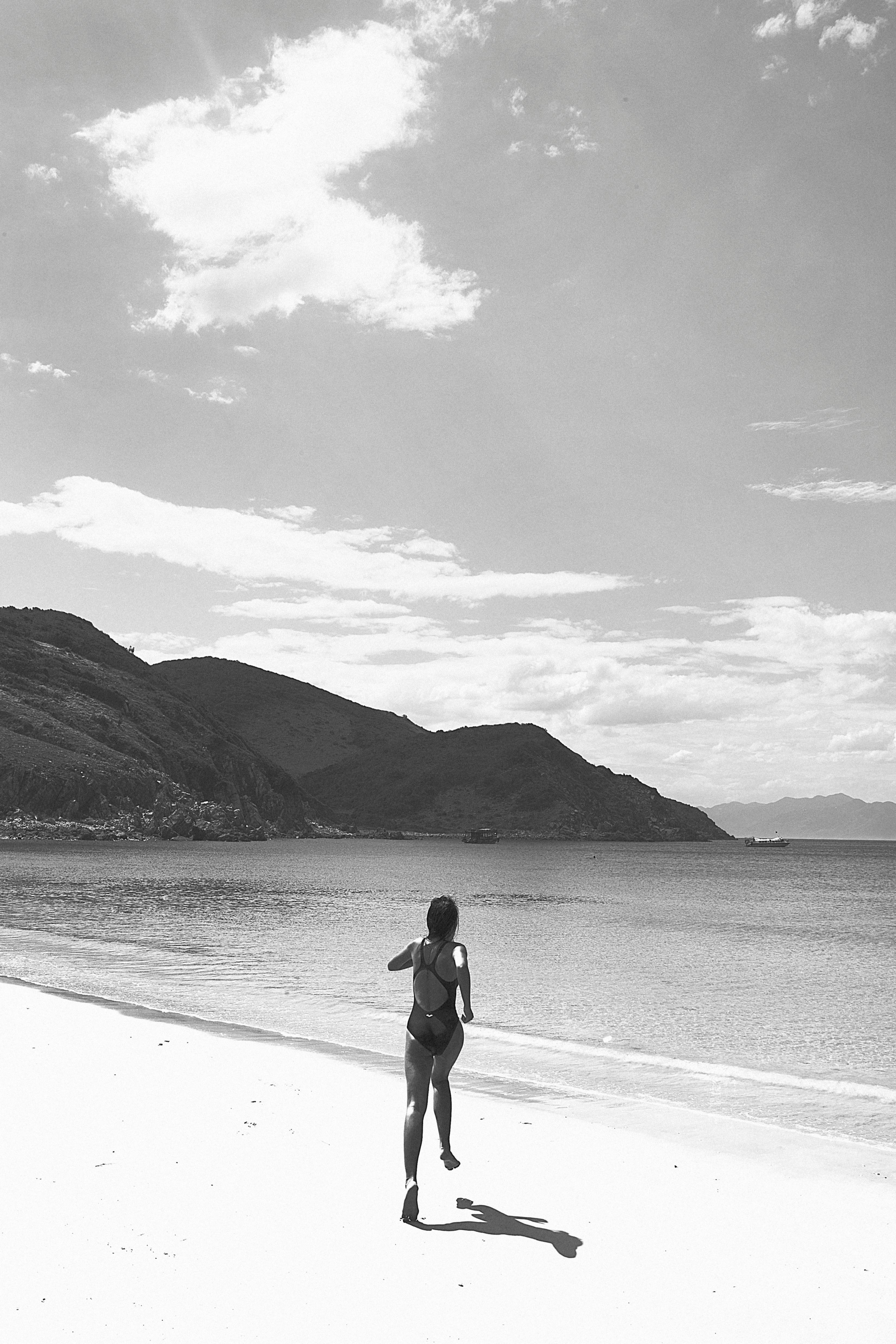 A woman running on a serene beach in Nha Trang, Vietnam, captured in monochrome.