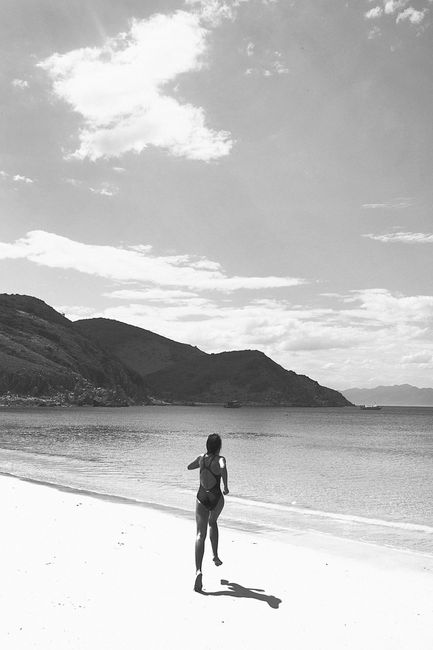 A woman running on a serene beach in Nha Trang, Vietnam, captured in monochrome.