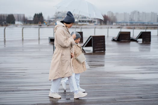 Side view of a woman and child walking together under an umbrella on a wet boardwalk.