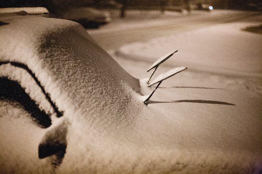 A car covered in snow with raised wipers during a cold winter night.