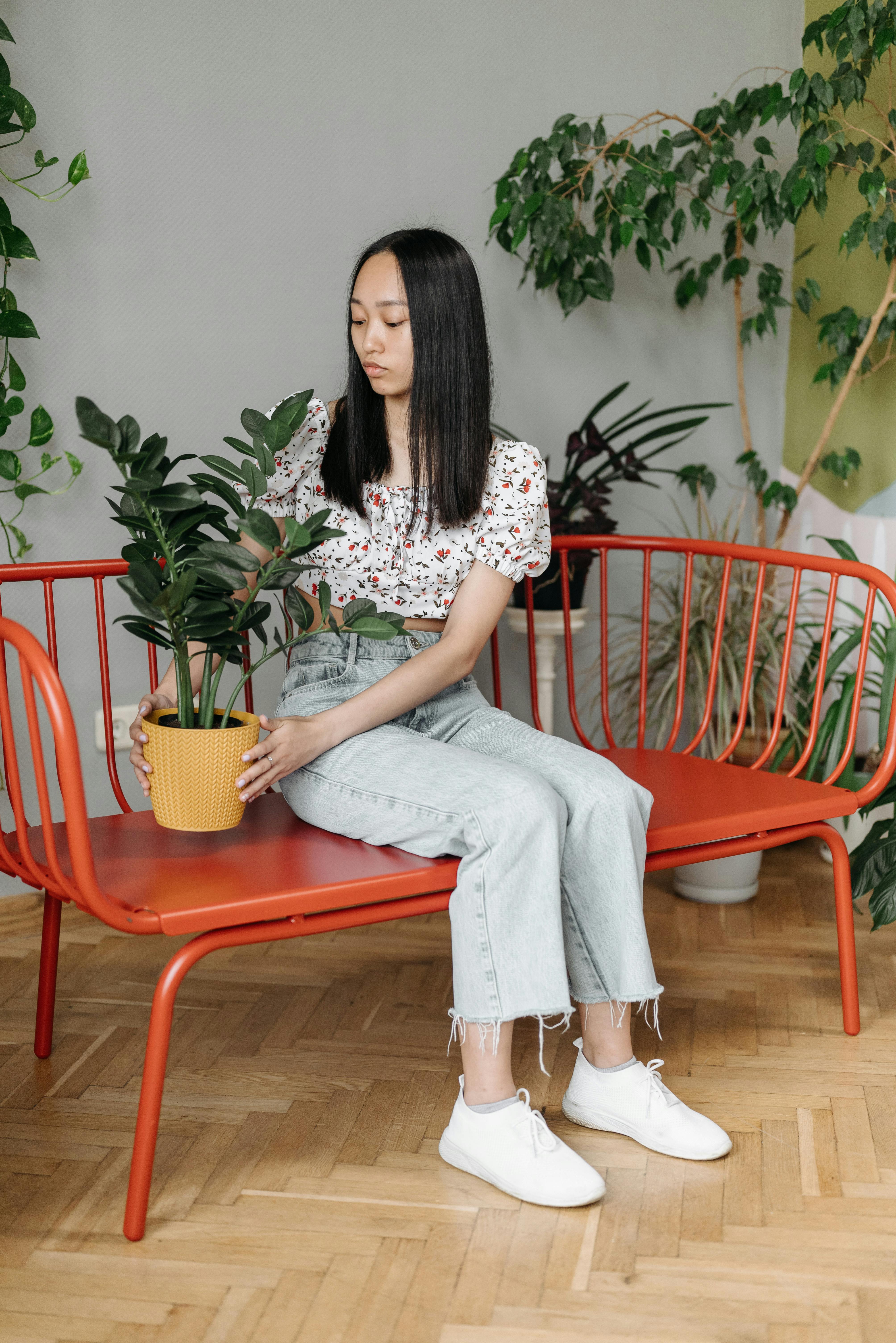 woman in white and red floral shirt and gray pants sitting on orange bench