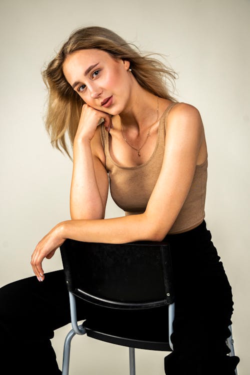 Woman in Brown Tank Top and Black Pants Sitting on Black Chair