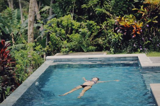 Woman floating in a serene pool amidst lush tropical plants, capturing a sense of relaxation and summer bliss.
