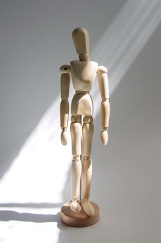 Wooden artist mannequin standing on a sunlit surface, casting soft shadows.