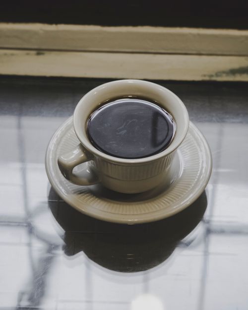 Free Close-up of a steaming cup of black coffee on a reflective table indoors. Perfect for morning themes. Stock Photo