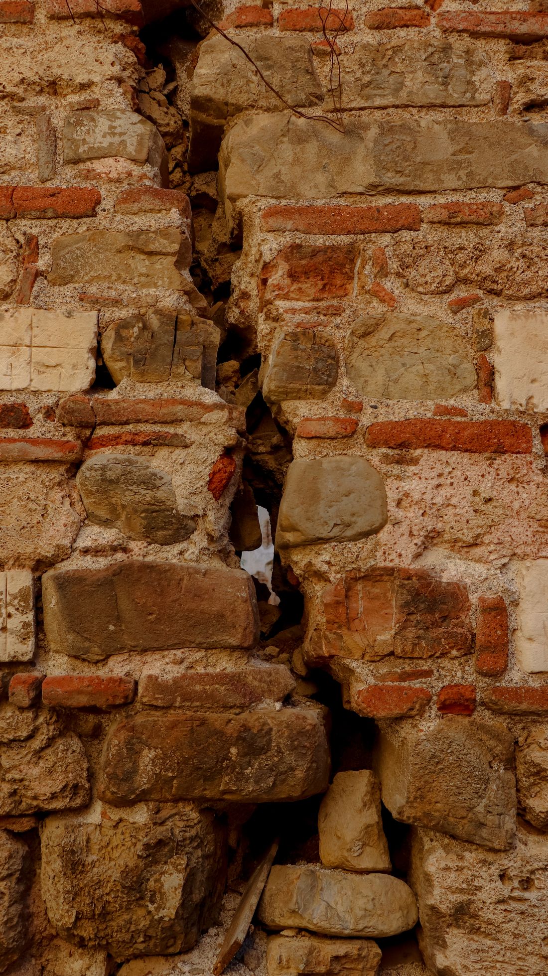 Mur ancien en pierre et brique avec une fissure et des joints dégradés