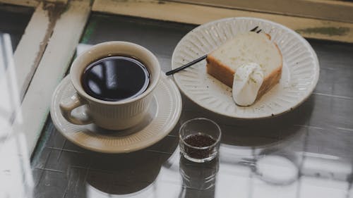 A Cup of Black Coffee Beside a Bread on a Plate