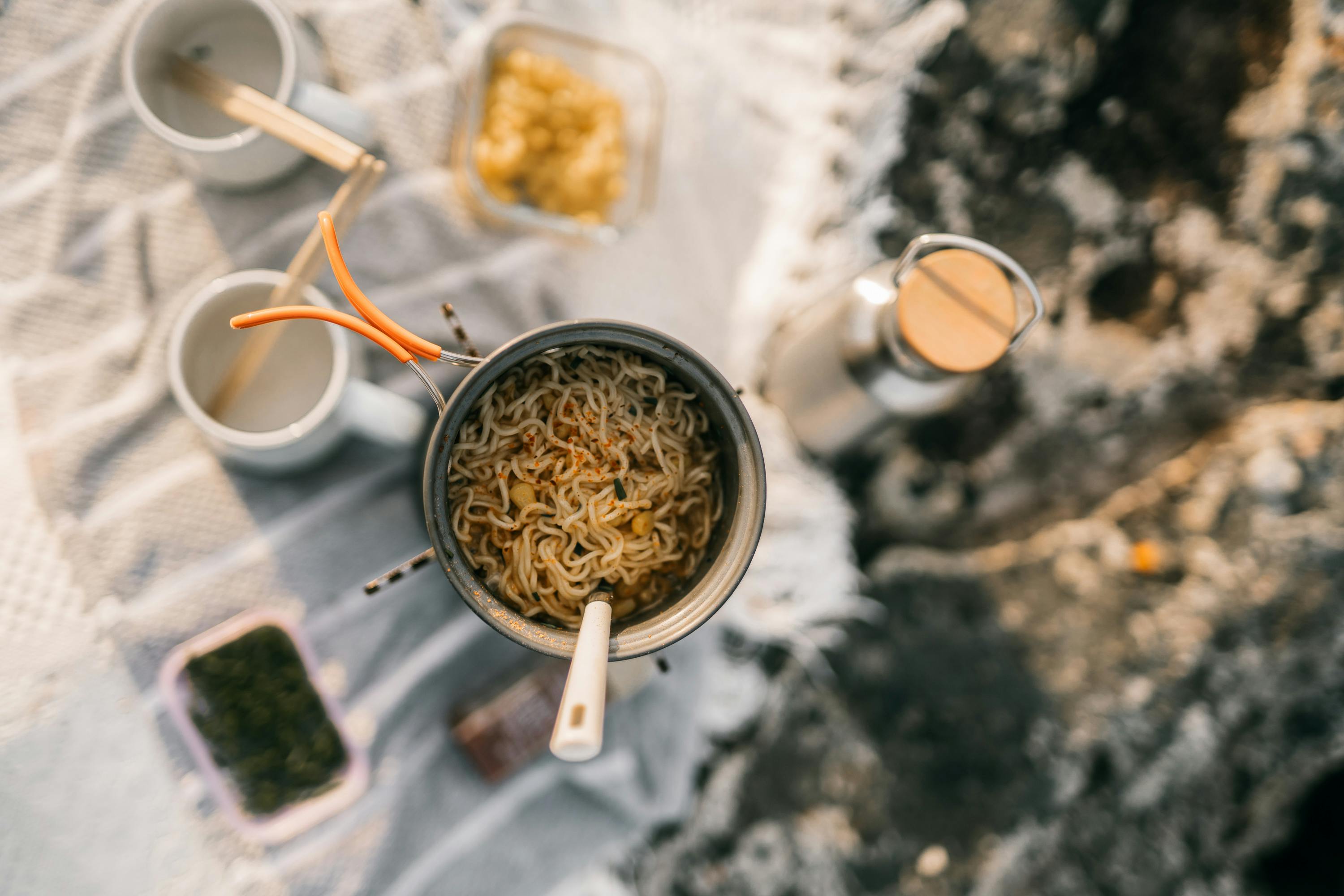 Top view of instant noodles cooking during a camping trip, with various outdoor kitchen essentials.
