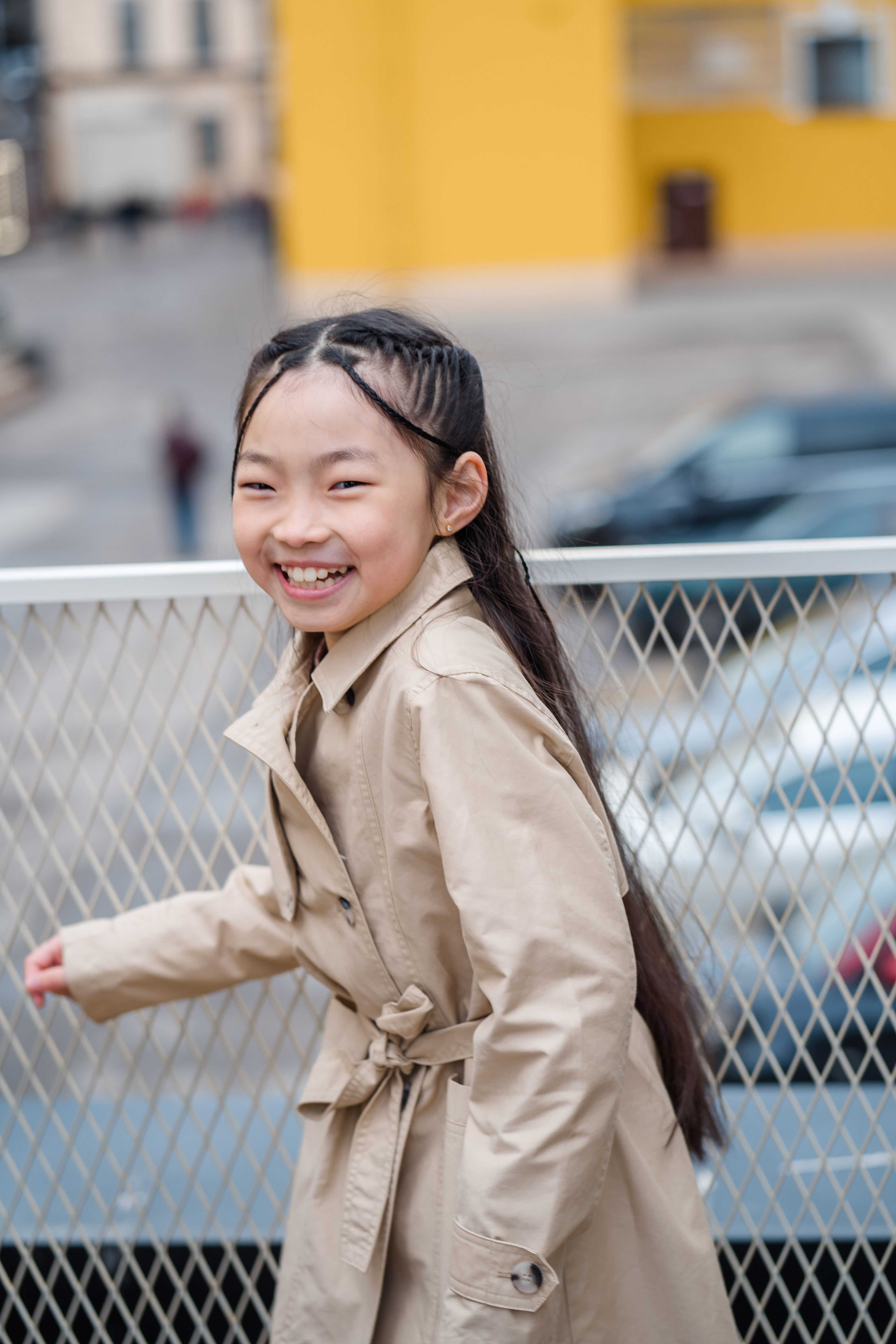 Happy girl in a beige coat smiling outdoors with a blurred background.