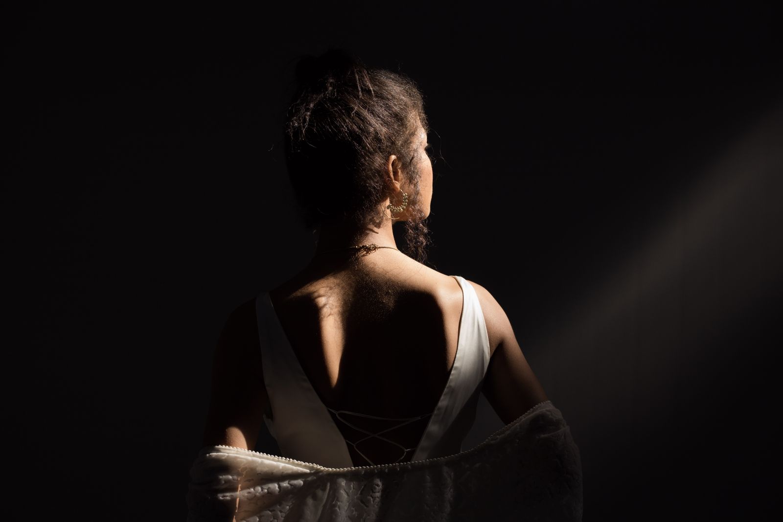 Woman seen from behind in a white dress, lit by a warm beam of light against a dark background