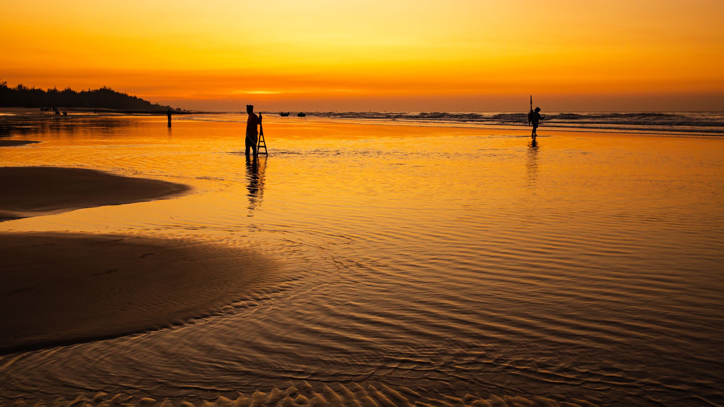Silhouetted fishermen at Hồ Tràm, Vietnam during a golden sunset. Peaceful and tranquil scene.