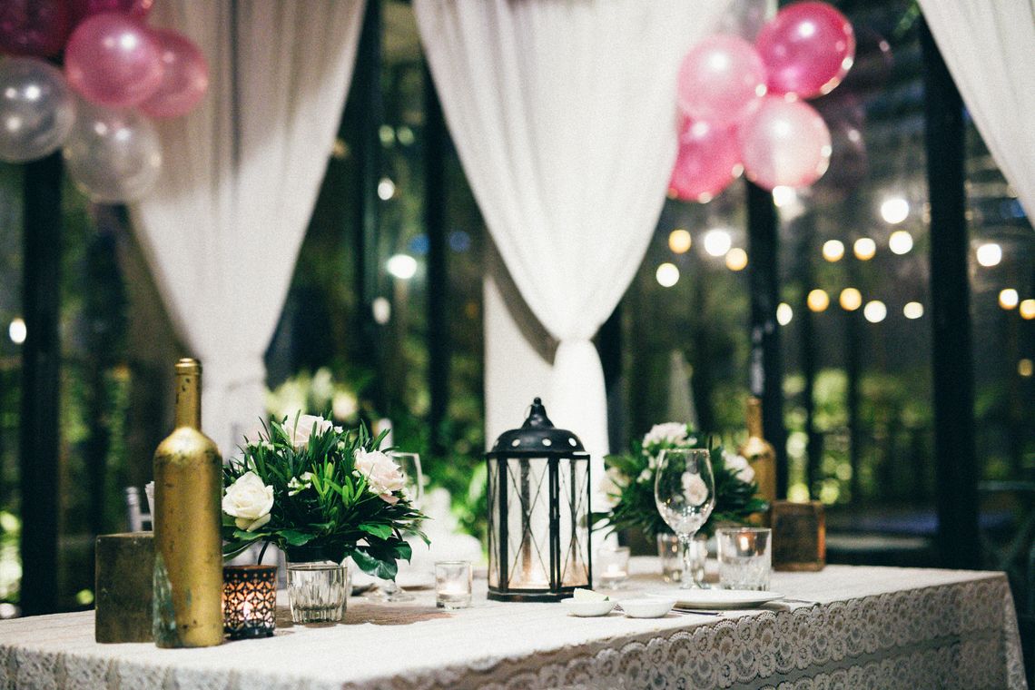Elegant celebration table with lanterns, flowers, balloons, glassware, and warm ambient decor