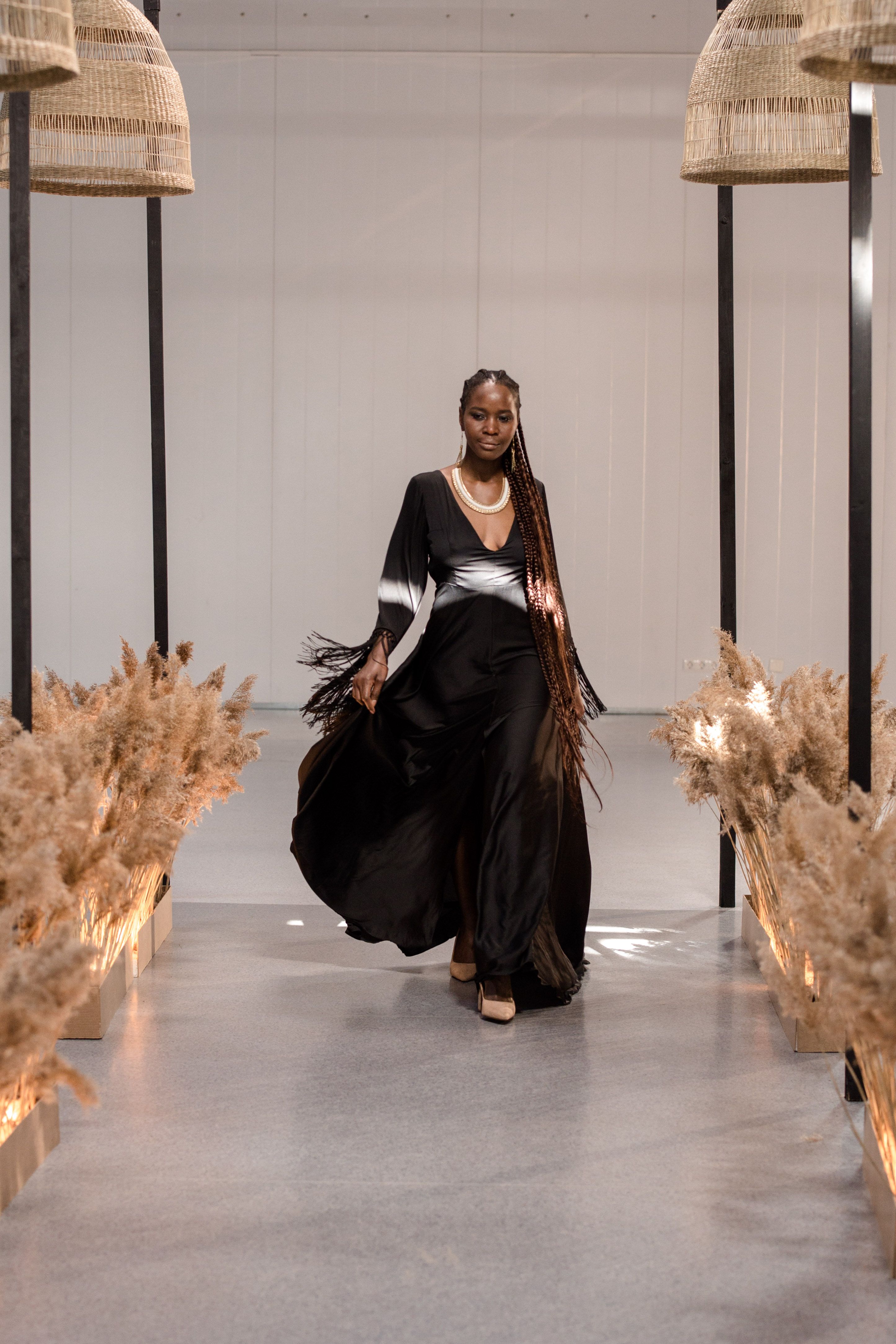 Mulher negra em um deslumbrante vestido preto na passarela de um desfile de moda dentro de um ambiente fechado.