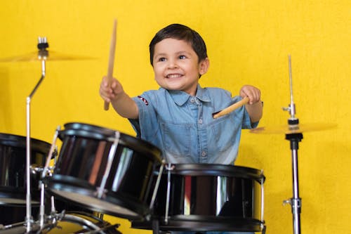A Little Boy in Denim Shirt Playing Drums