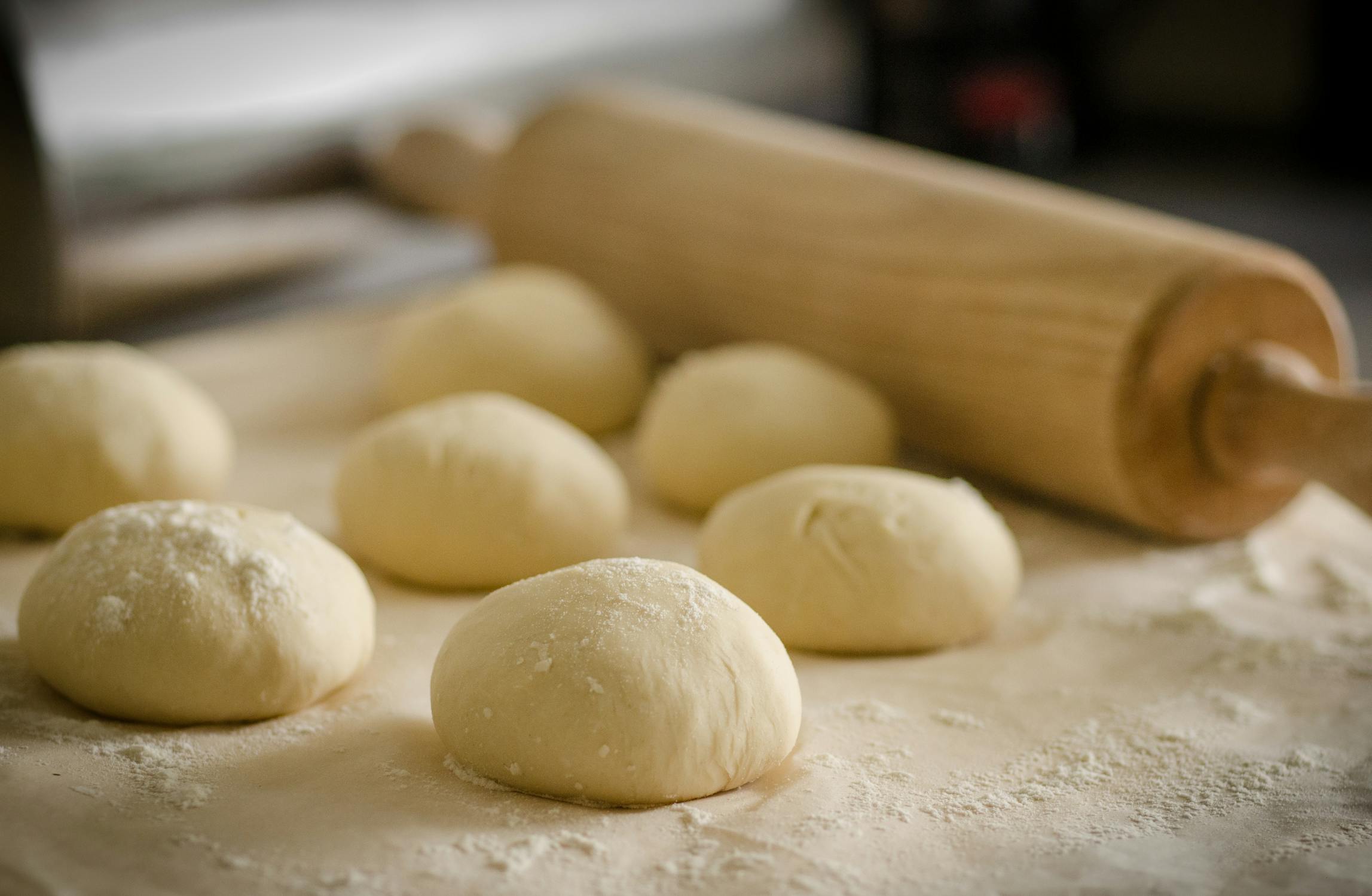 Balls of dough sit on a baking tray with a rolling pin in the background. Photo by Skitterphoto. Used courtesy of Pexels.com.