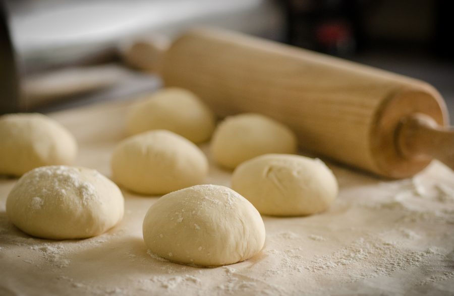 Soft balls of fresh dough resting on a floured surface next to a wooden rolling pin