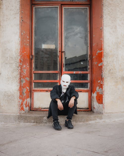 A Man in a Ski Mask Sitting at the Entrance of a Building