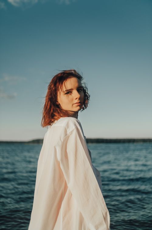 Free A woman with red hair looking at the camera during a sunny day by the sea. Stock Photo