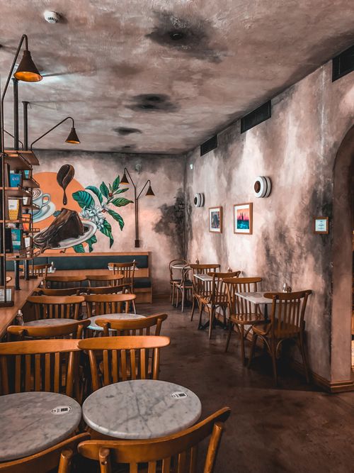 Free Warm and inviting cafe interior featuring wooden furniture, art mural, and ambient lighting for a relaxed atmosphere. Stock Photo