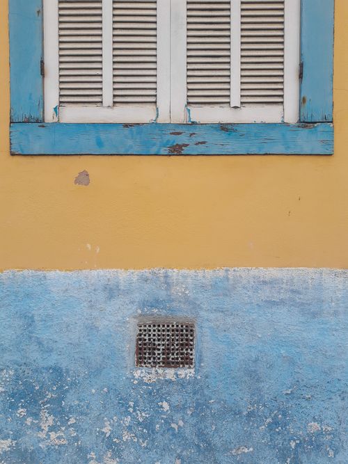 Free A rustic window set against a vibrant yellow and blue textured wall with peeling paint. Stock Photo