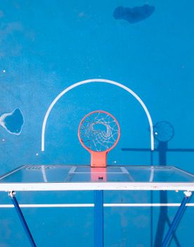A top view of a basketball hoop casting a shadow on a vibrant blue court.