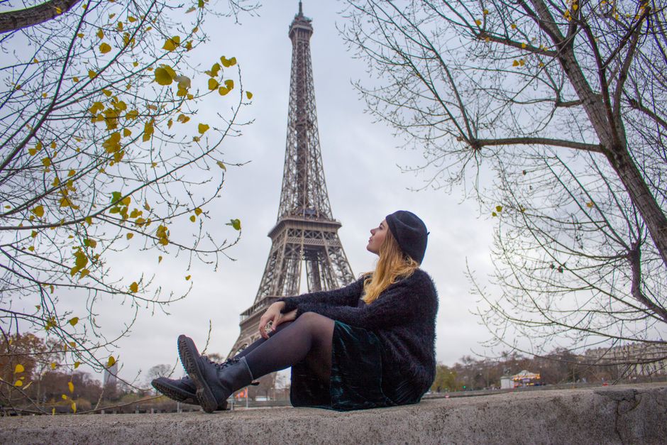 A woman in a stylish outfit sits contemplatively near the Eiffel Tower during fall in Paris.