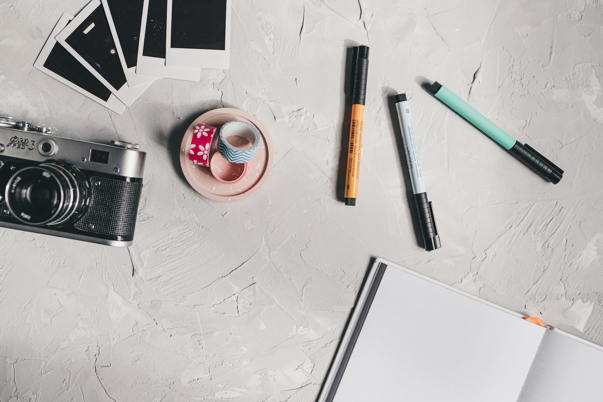 Flat lay of a creative workspace featuring a camera, pens, washi tape, and Polaroids.