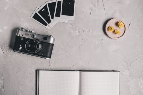 Free A vintage camera and polaroids on a textured desk with an open notebook and flowers. Stock Photo