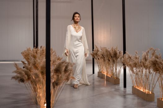 Model walks gracefully in a white gown amidst elegant decor, highlighting indoor fashion aesthetics.