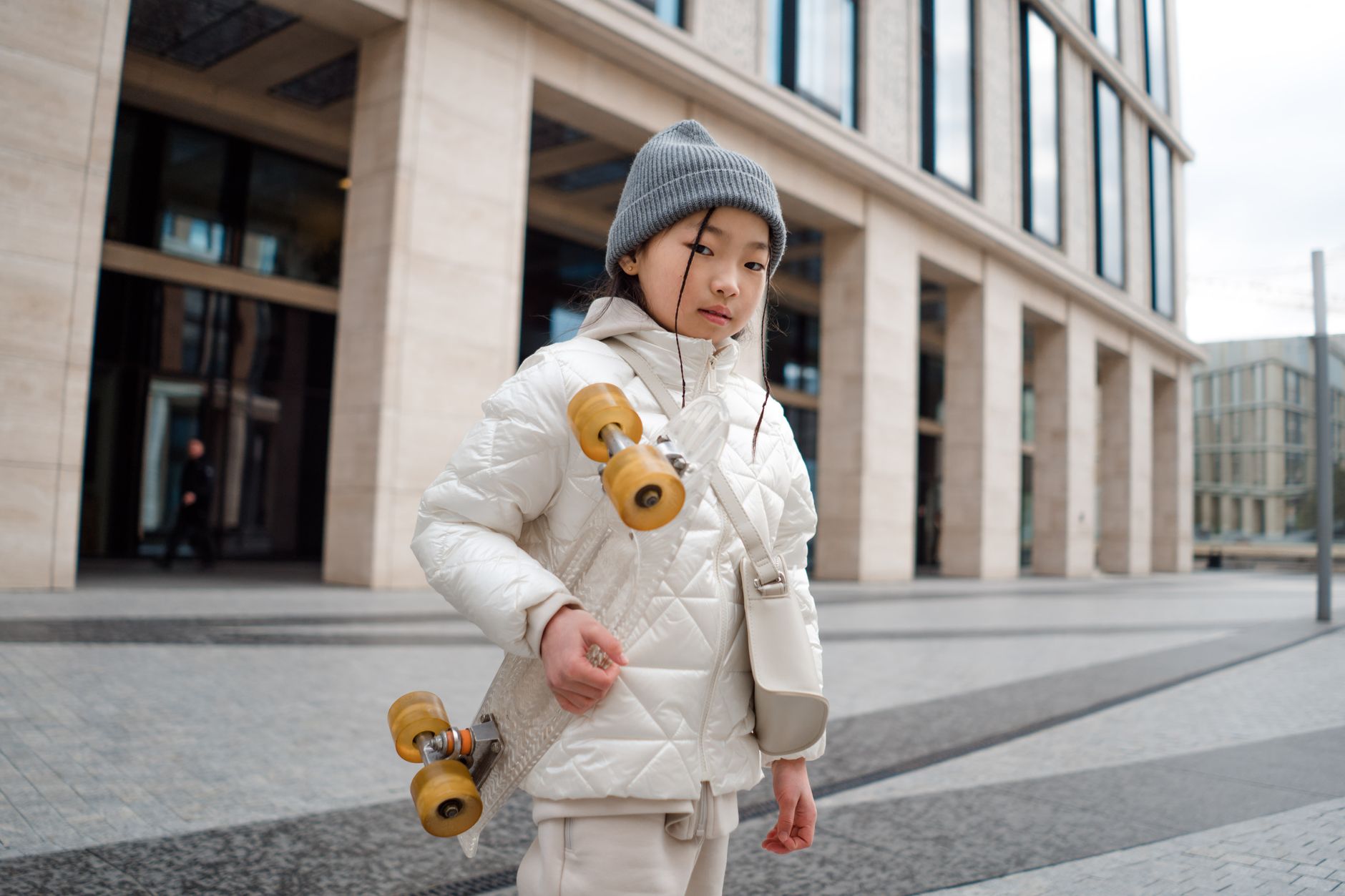 Jeune fille en veste matelassée blanche avec skateboard dans un quartier moderne