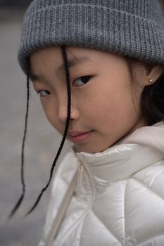 Close-up portrait of a young girl wearing a gray beanie and a white jacket.