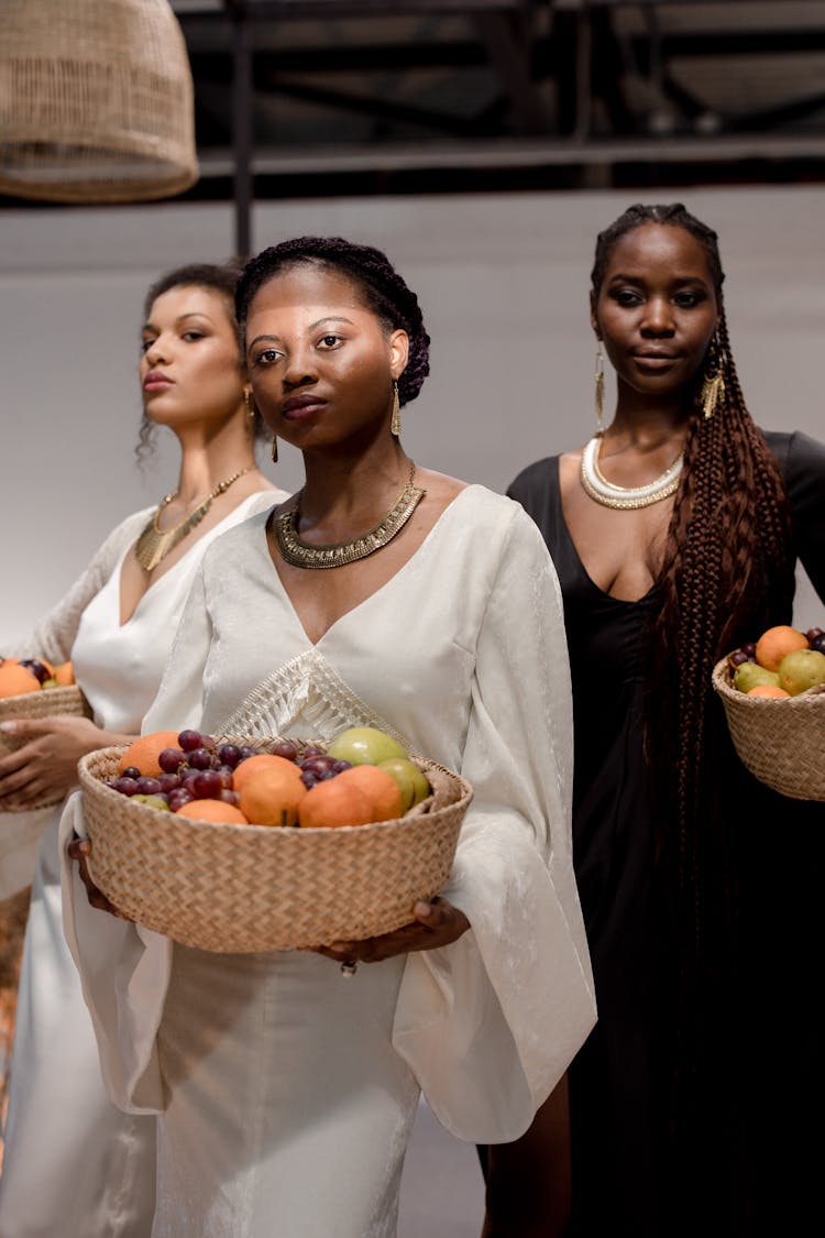 Photograph Of Women Holding Baskets With Fruits