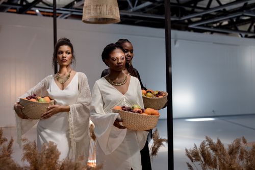 Free Three elegantly dressed women in a well-lit indoor setting carrying fruit baskets, embodying modern fashion and culture. Stock Photo