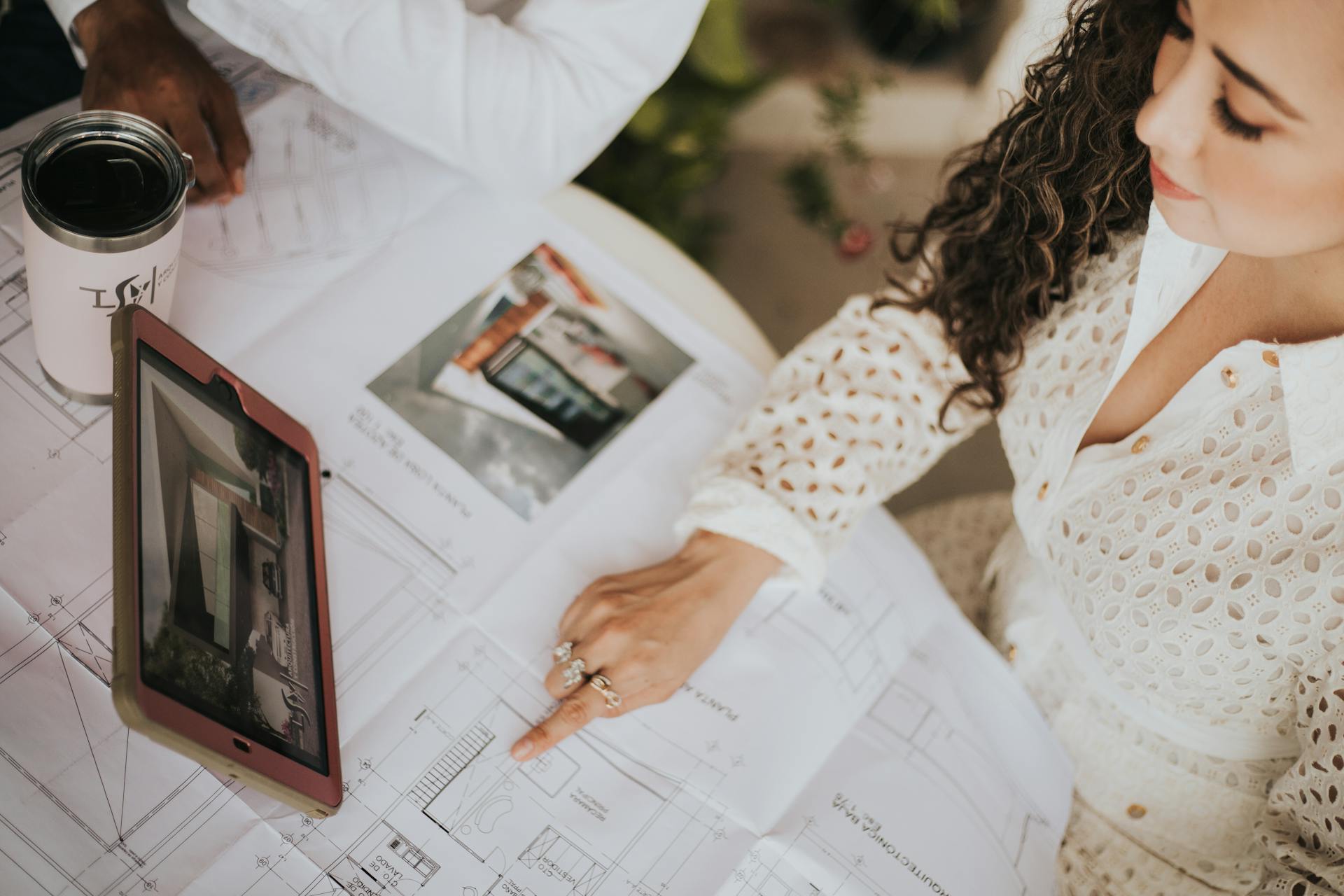 A woman reviews architectural floor plans on a table with a tablet in a modern workspace.