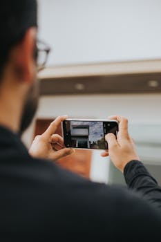 A man takes a picture of modern architecture with a smartphone outdoors.
