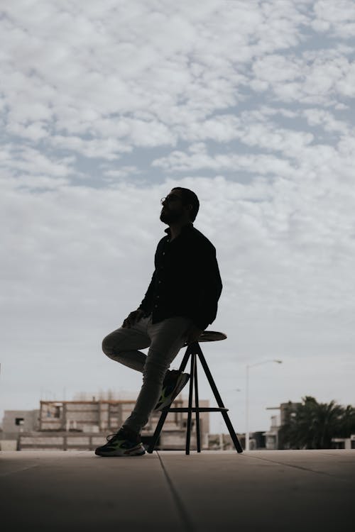 Man in Black Long Sleeves Shirt Sitting on a Stool Under a Cloudy Sky