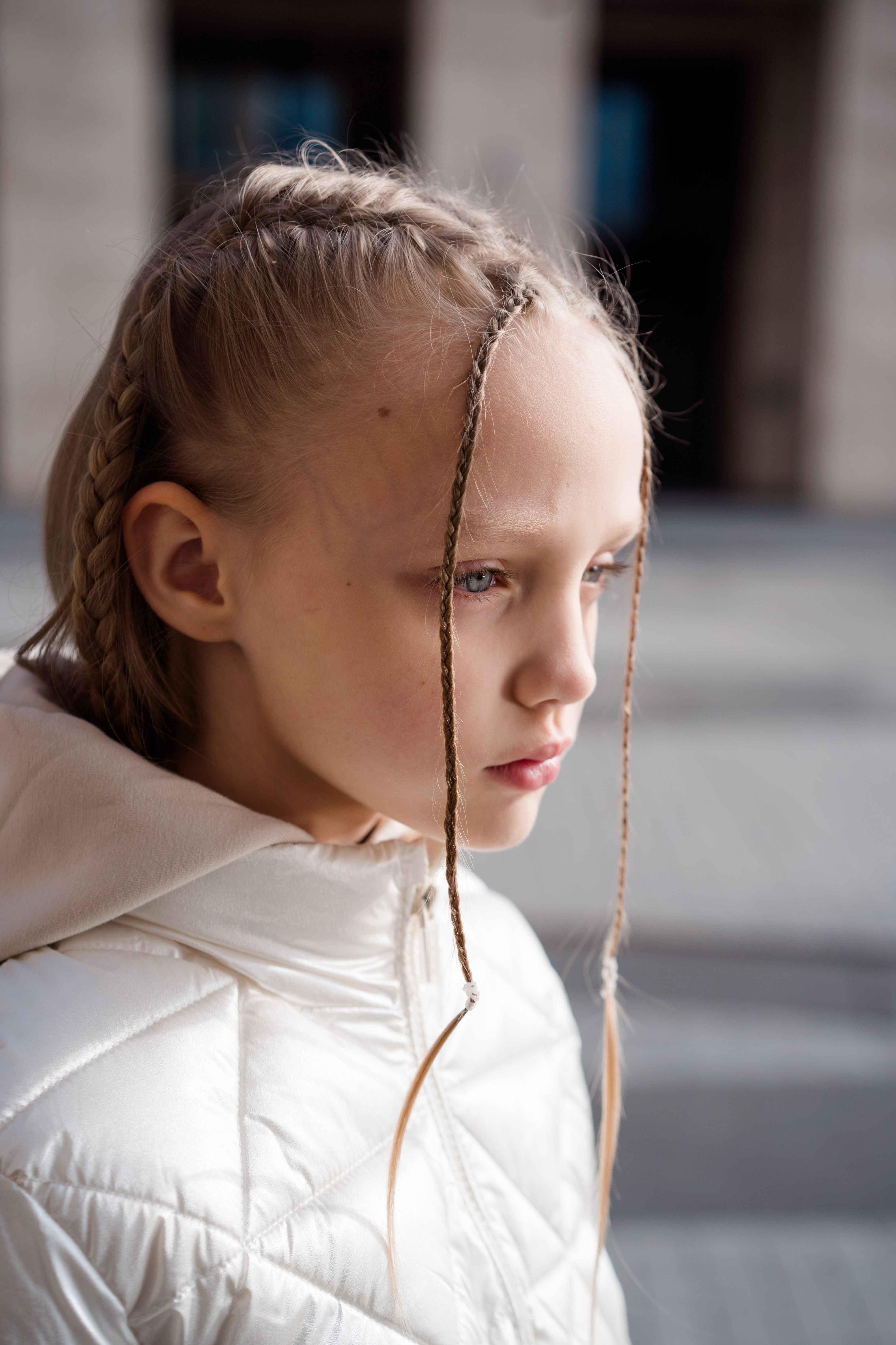 Young girl with braided hair looking thoughtful in an urban setting.
