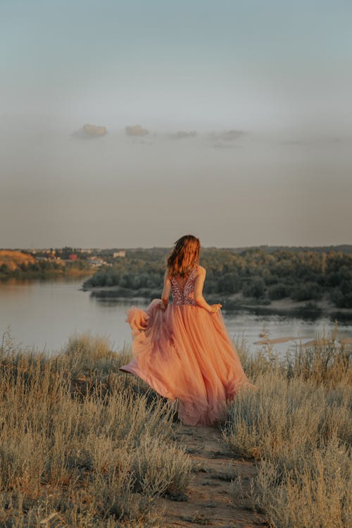 Woman in Brown Dress Sitting on Grass Field Near Lake